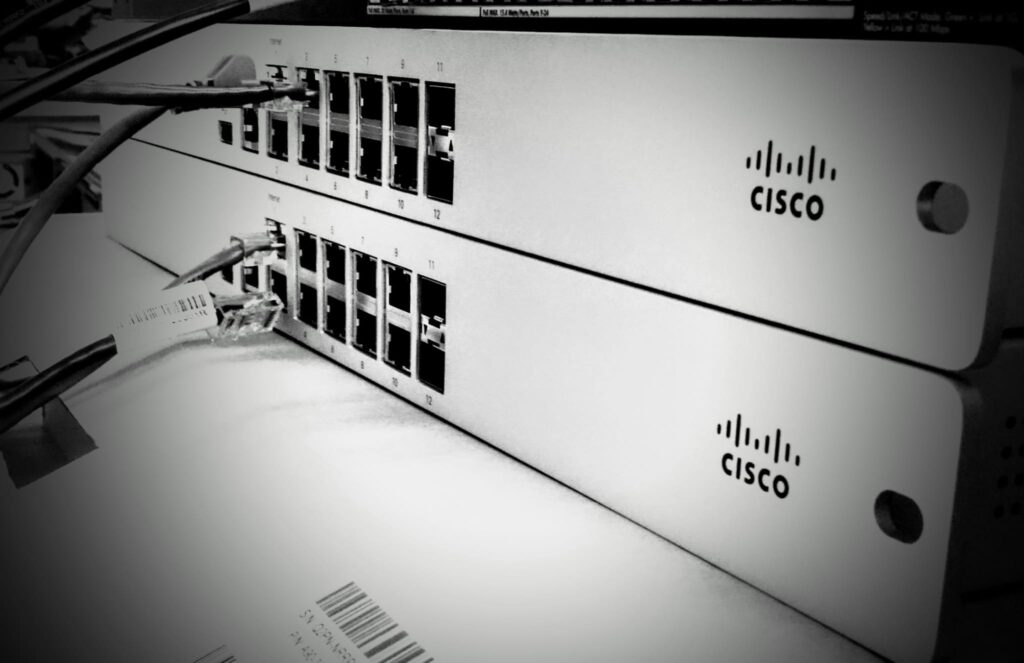 A black and white styled photo of 2 cisco network switches A black and white styled photo of 2 cisco network switches